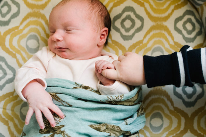 baby girl holding finger of toddler big brother