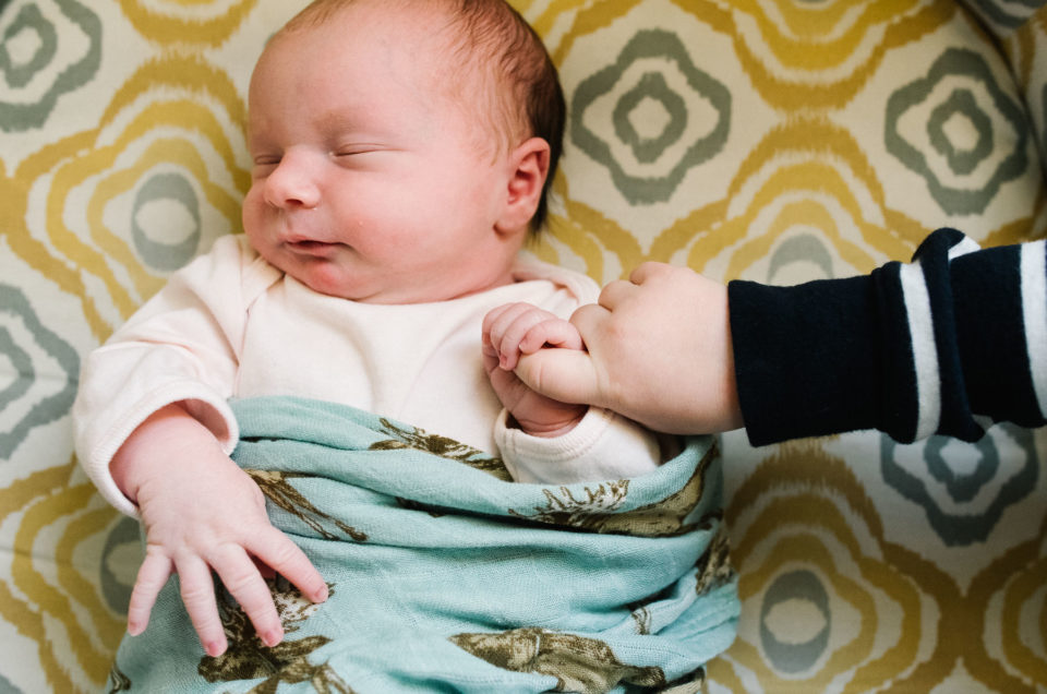 baby girl holding finger of toddler big brother