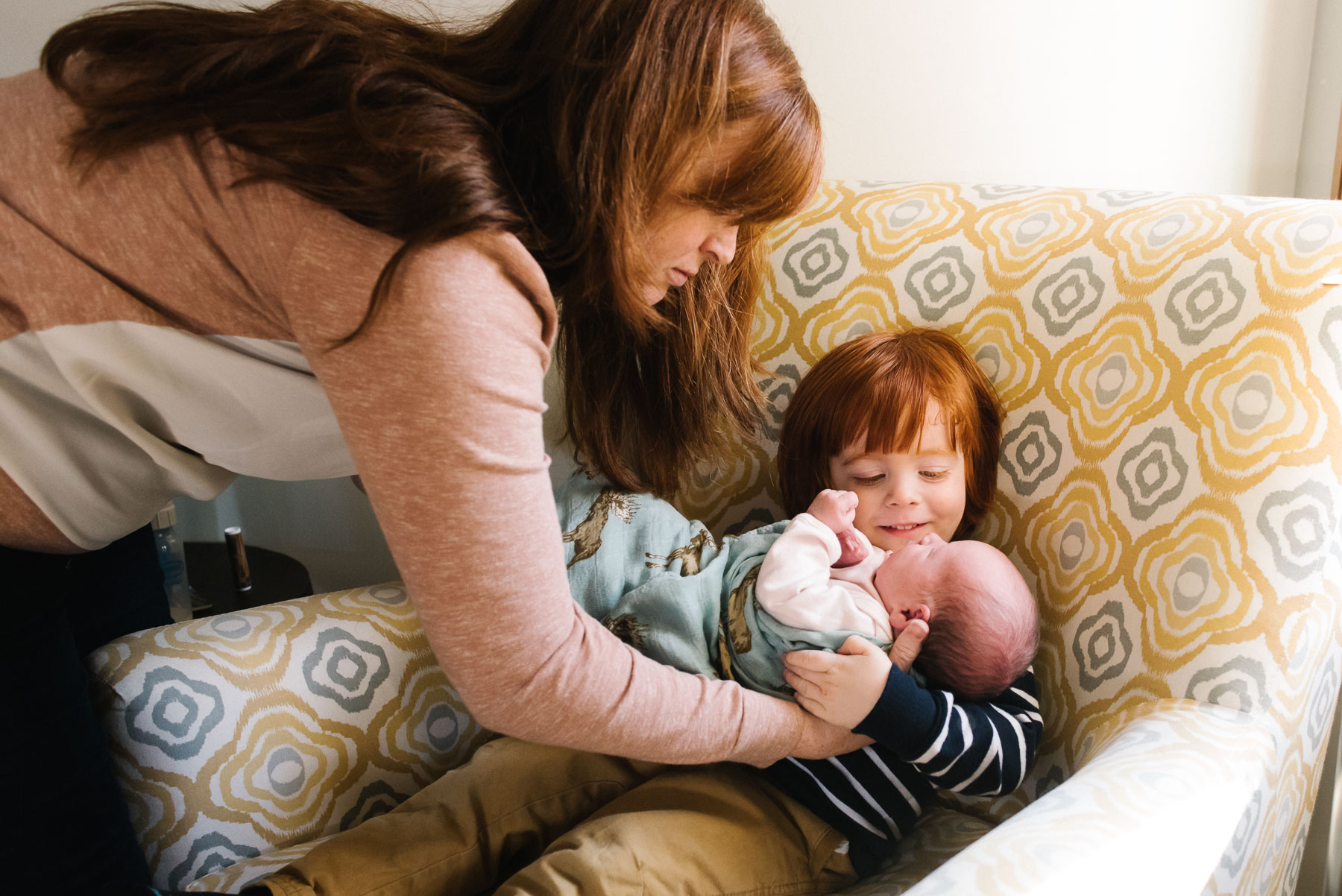 mom handing newborn baby girl to toddler son