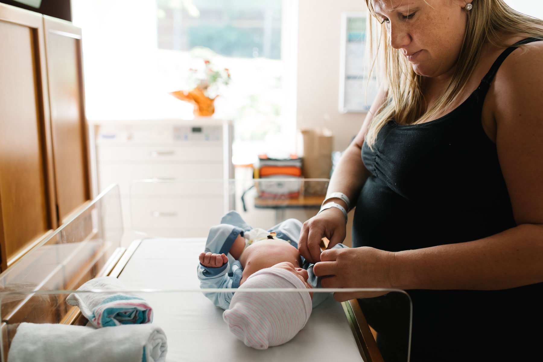 mom dressing newborn baby in onesie at hospital