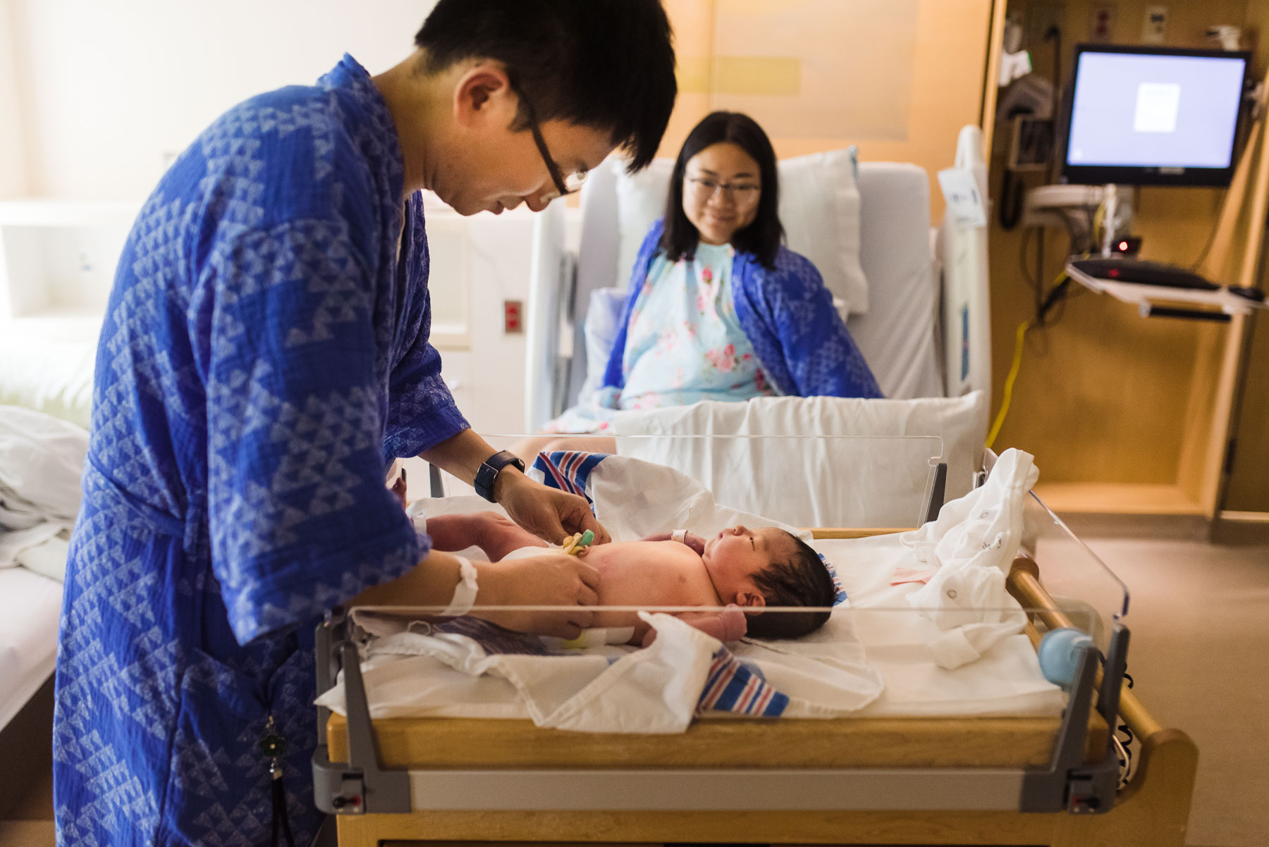 dad changing baby's diaper in hospital while mom looks on