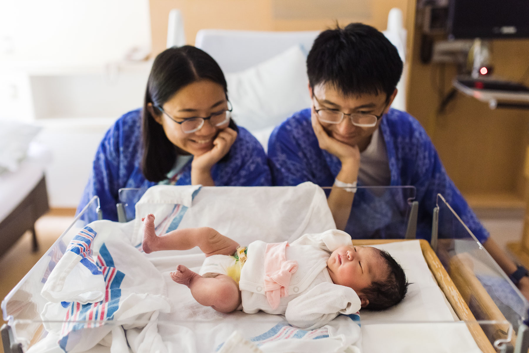 parents smiling at newborn baby in bassinet