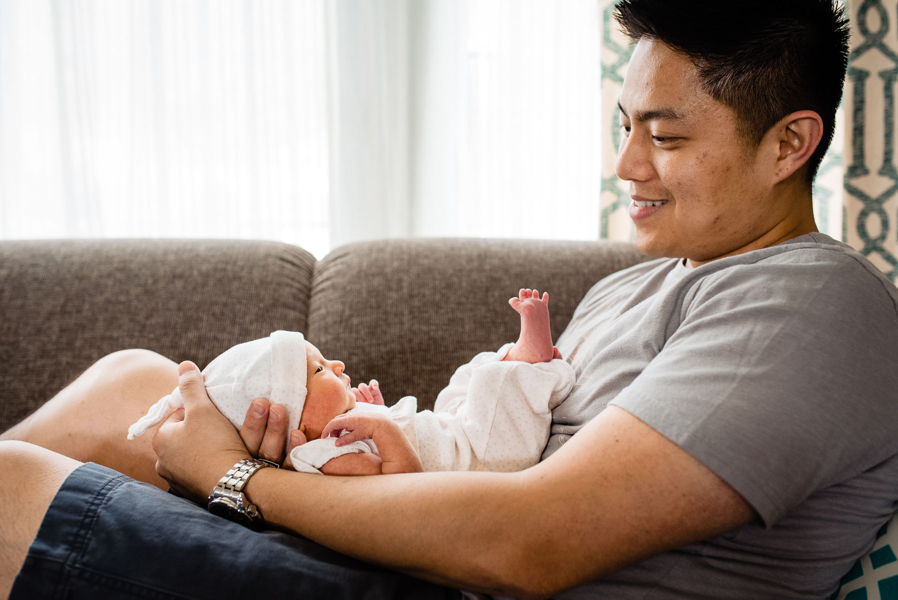 asian father relaxing with newborn baby on couch