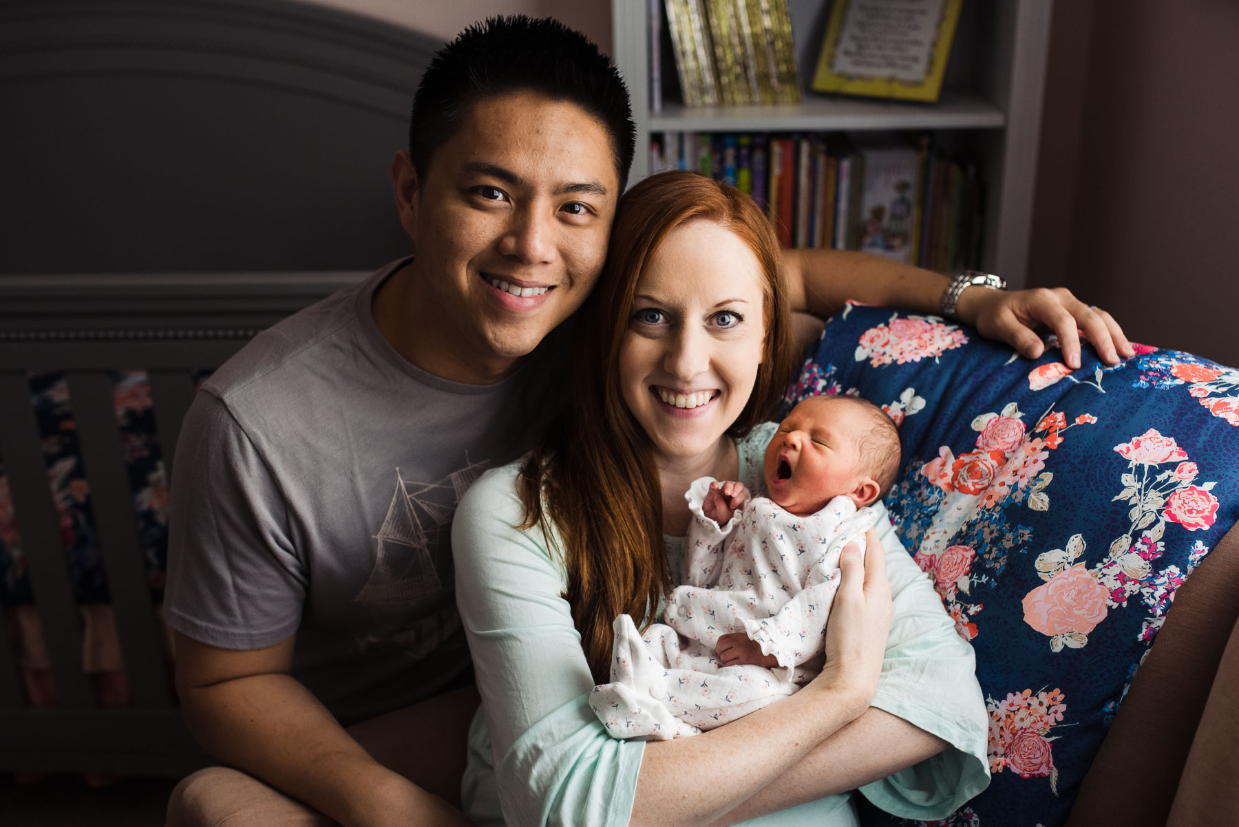 asian male and red haired caucasian mother with newborn baby girl in home nursery