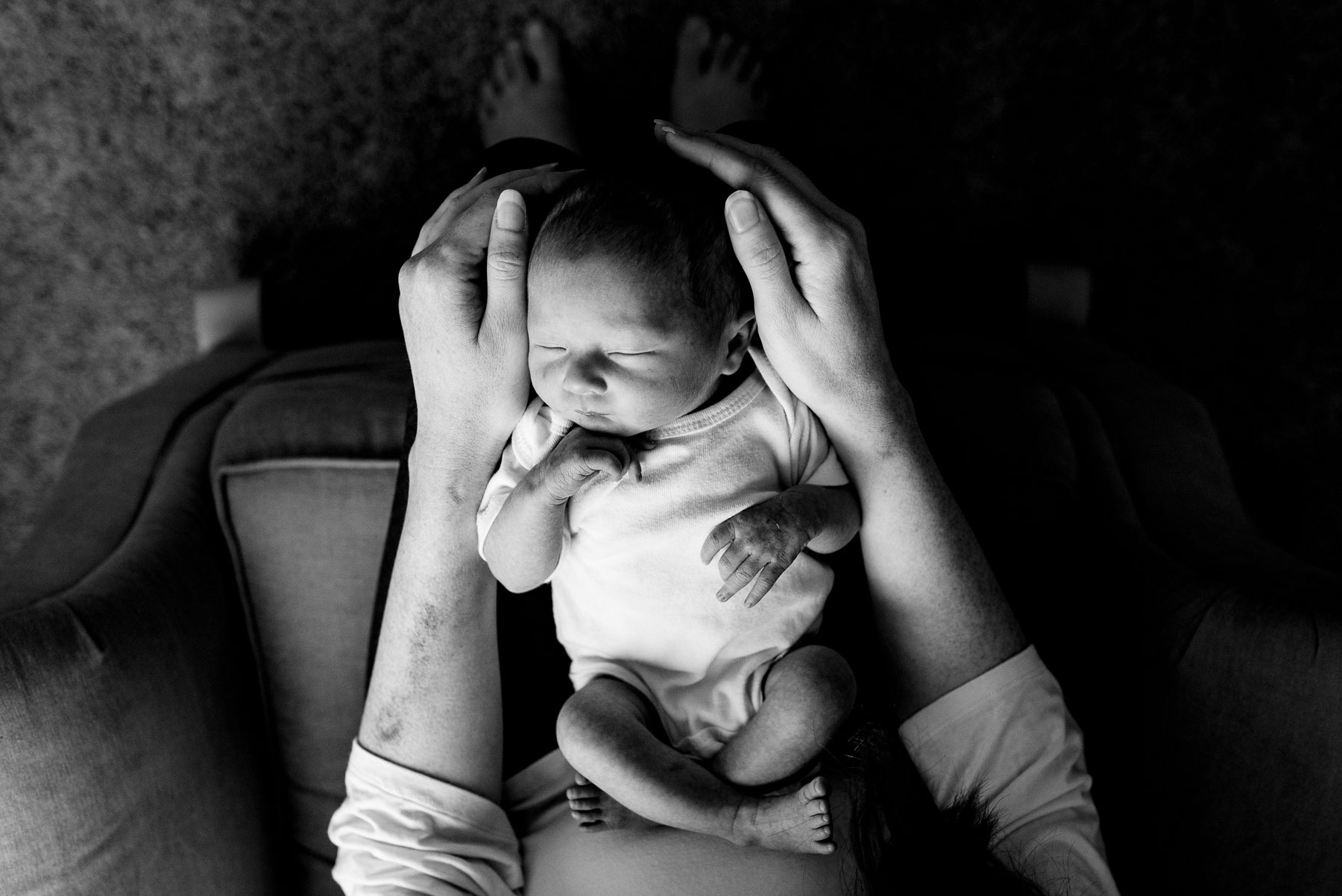 black and white photo of newborn baby in mother's lap with mother's arms around her
