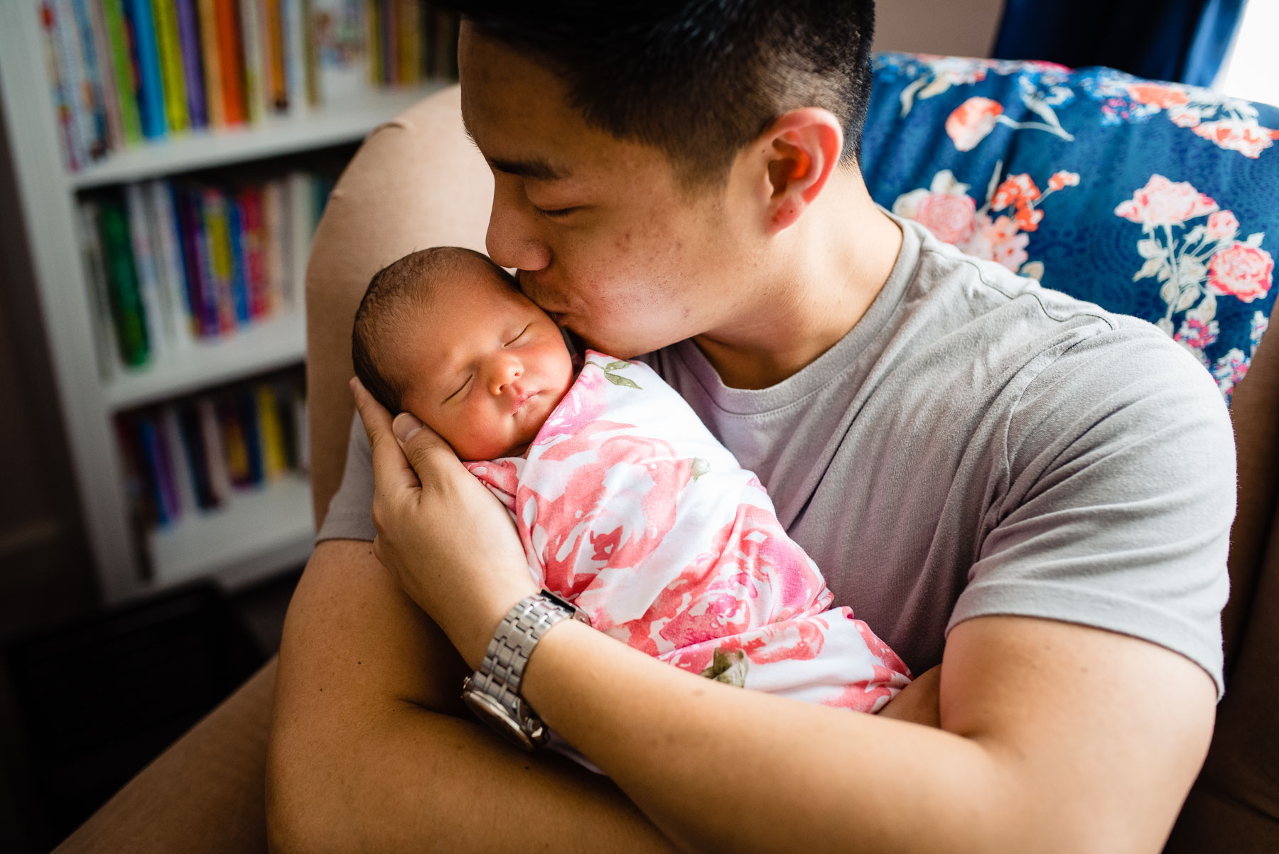 asian father holding and kissing his newborn baby girl