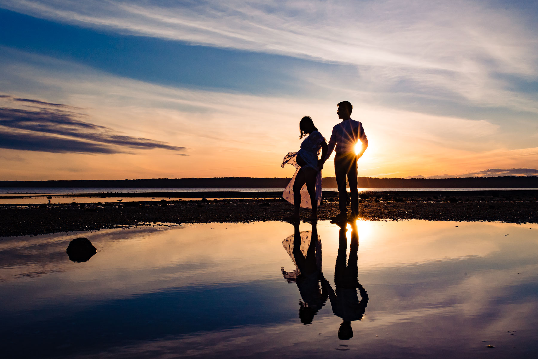 sunset silhouette of expecting couple at beach with reflection in water