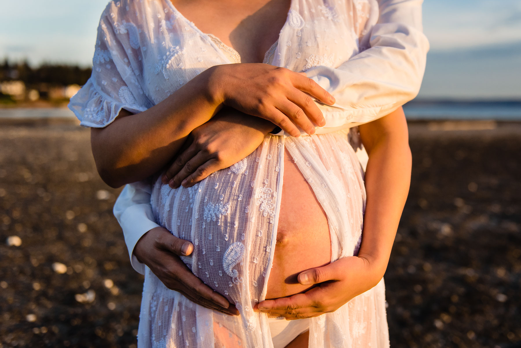 close up of pregnant belly with couple's arms around it