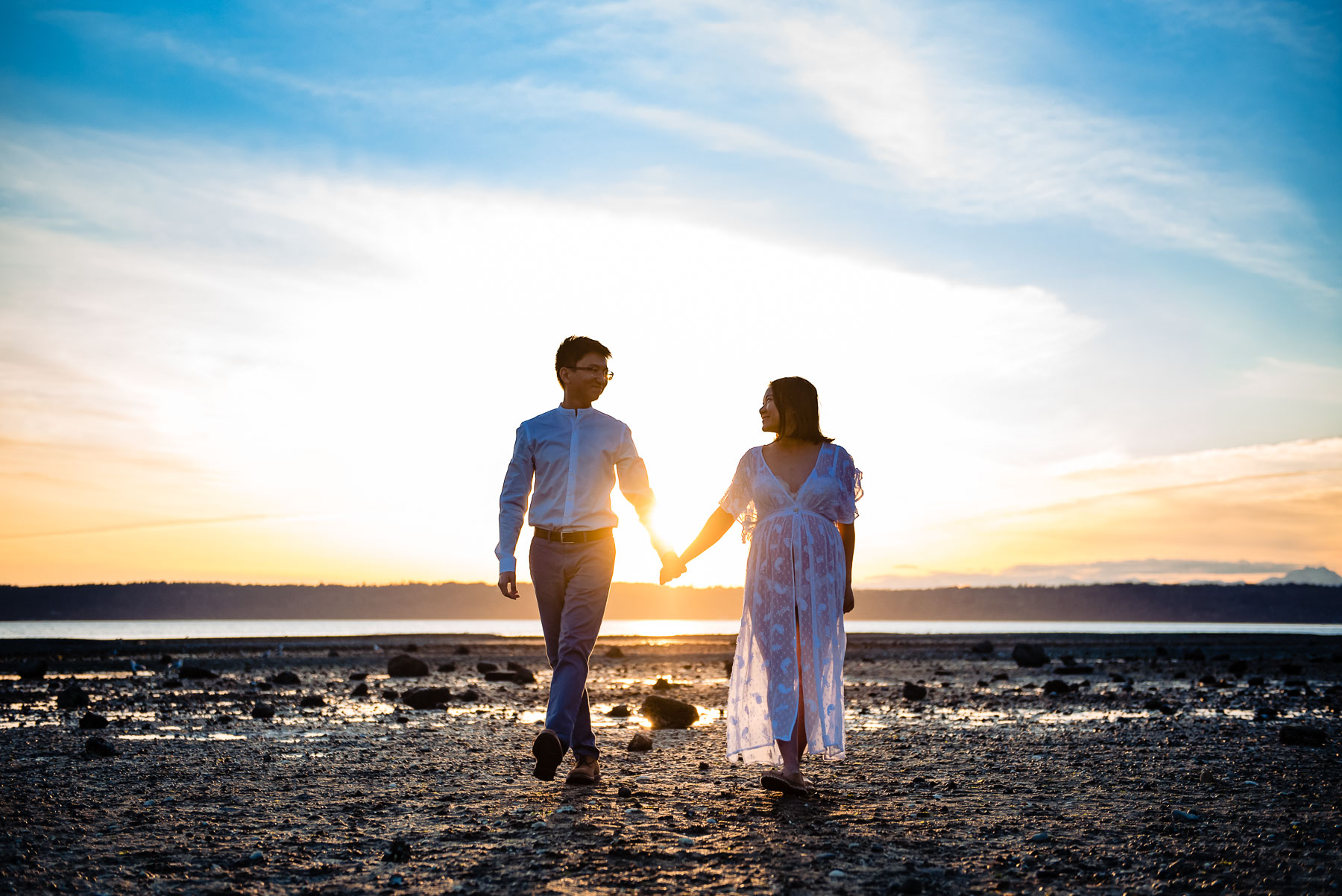 Asian couple and pregnant wife holding hands walking at beach