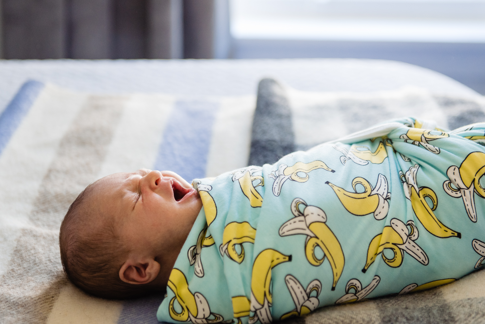 newborn baby yawning on bed in banana swaddle