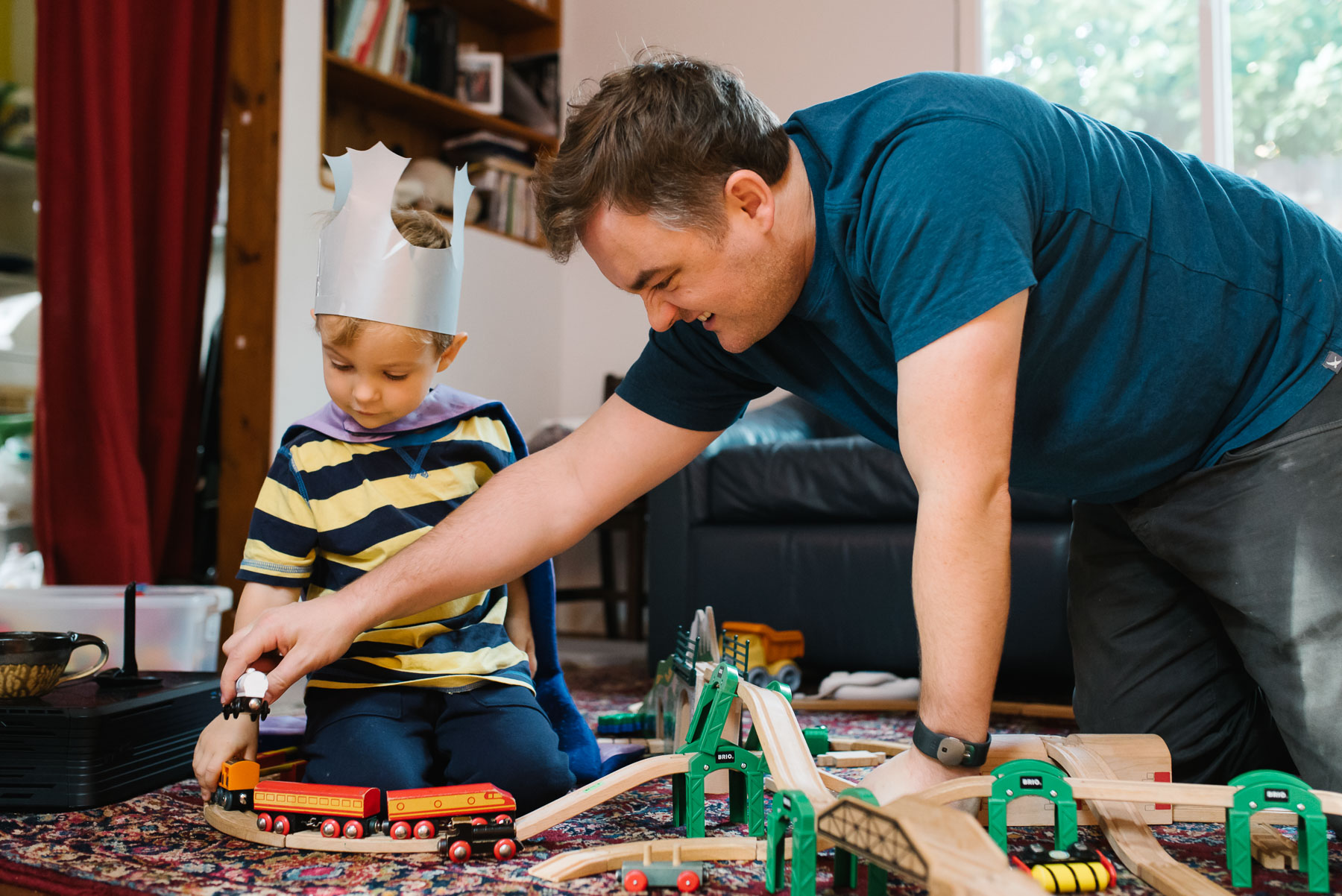 father playing train set with toddler son at home