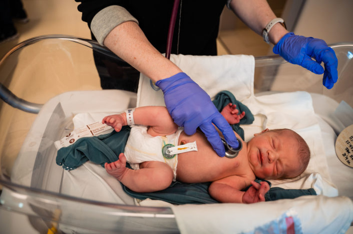 pediatrician listening to lungs of newborn baby in hospital bassinet